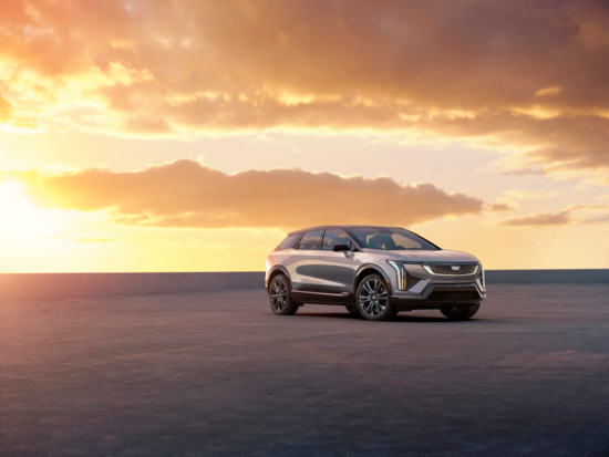 Sleek silver SUV parked on a vast concrete surface during sunset. The golden sky with scattered clouds casts a warm glow, creating a serene ambiance.